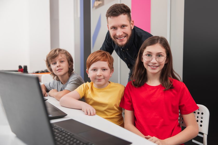 junger Lehrer mit 3 Schülern am Laptop