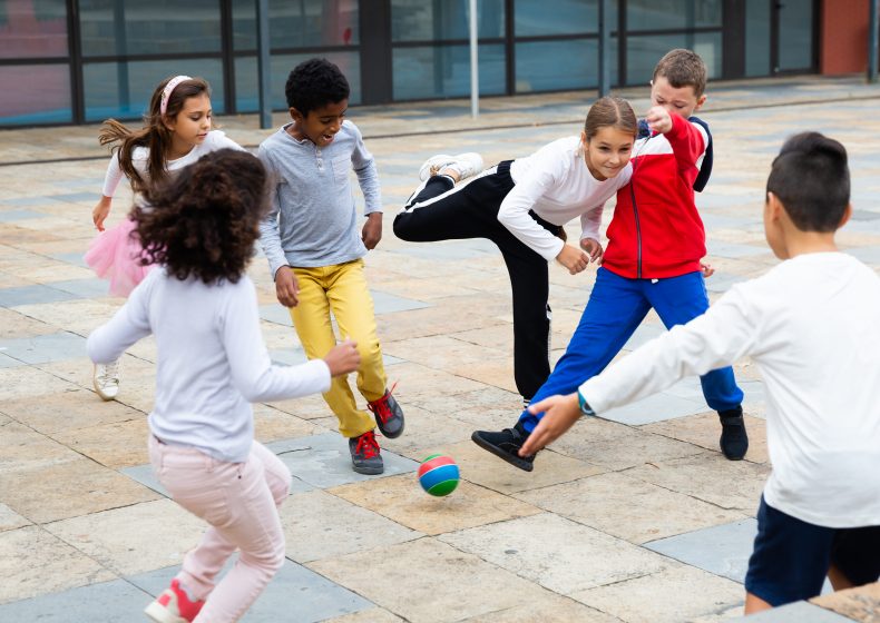 Gruppe aktiver Schüler, die am Sommertag Fußball spielen