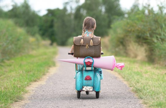 Erster Schultag, glückliches Mädchen mit Roller auf dem Weg zur Schule