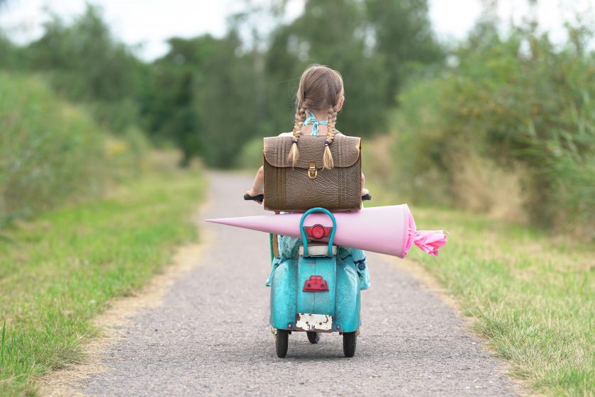 Erster Schultag, glückliches Mädchen mit Roller auf dem Weg zur Schule