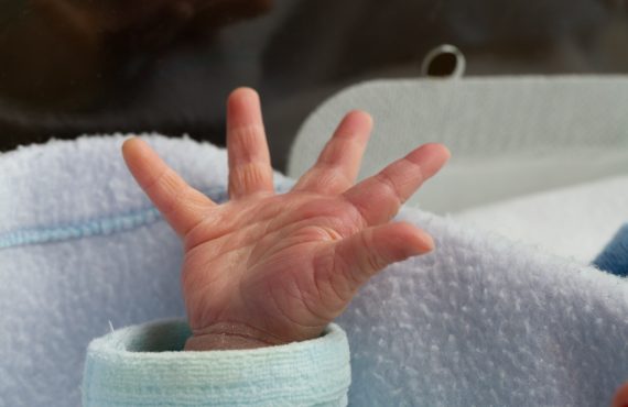 Die Hand des Neugeborenen streckt sich aus der Decke im Inkubator