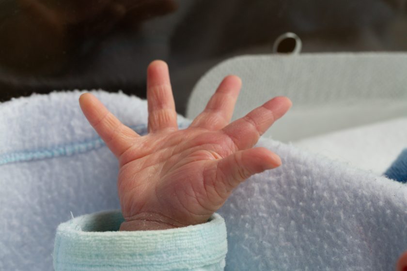 Die Hand des Neugeborenen streckt sich aus der Decke im Inkubator