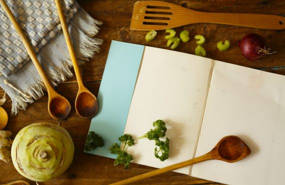 Kochbuch mit verschiedenen Gemüsen und Vintage-Küchenutensilien